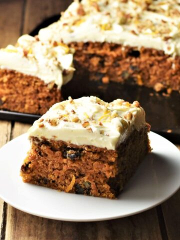 Side view of low fat carrot cake slice on white plate with cake in background.