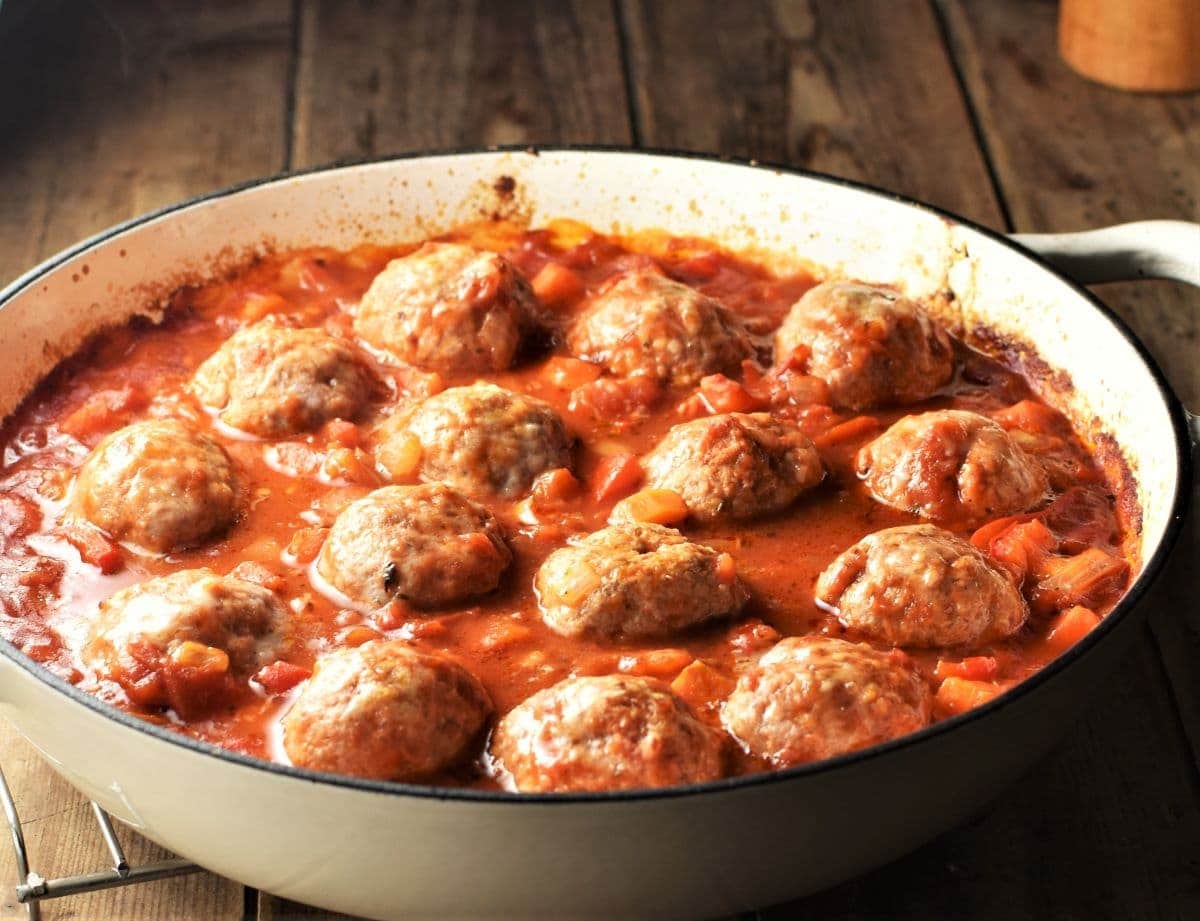 Side view of meatball casserole with vegetable sauce in white dish.