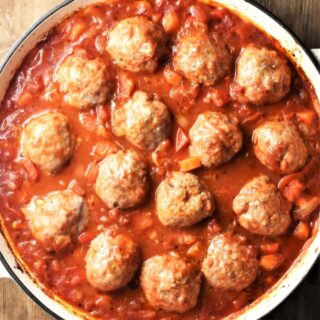 Top down view of meatballs in chunky vegetable sauce in white round dish.