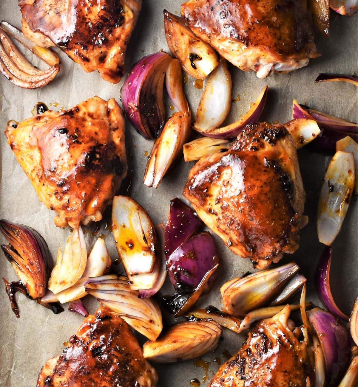 Chicken thighs and red onions with sticky glaze in sheet pan.