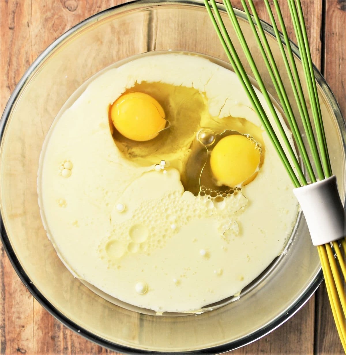 Milk and eggs in bowl with green whisk.