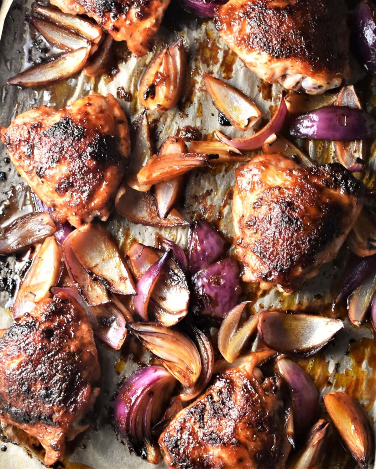 Roasted chicken pieces and onions on top of parchment.