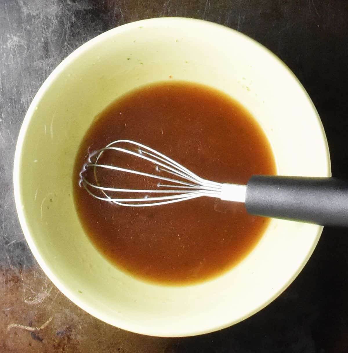 Top down view of sweet chili dressing in yellow bowl with whisk.