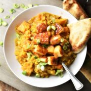 Top down view of sweet potato dahl with fried halloumi cubes in white bowl with naan and spoon.