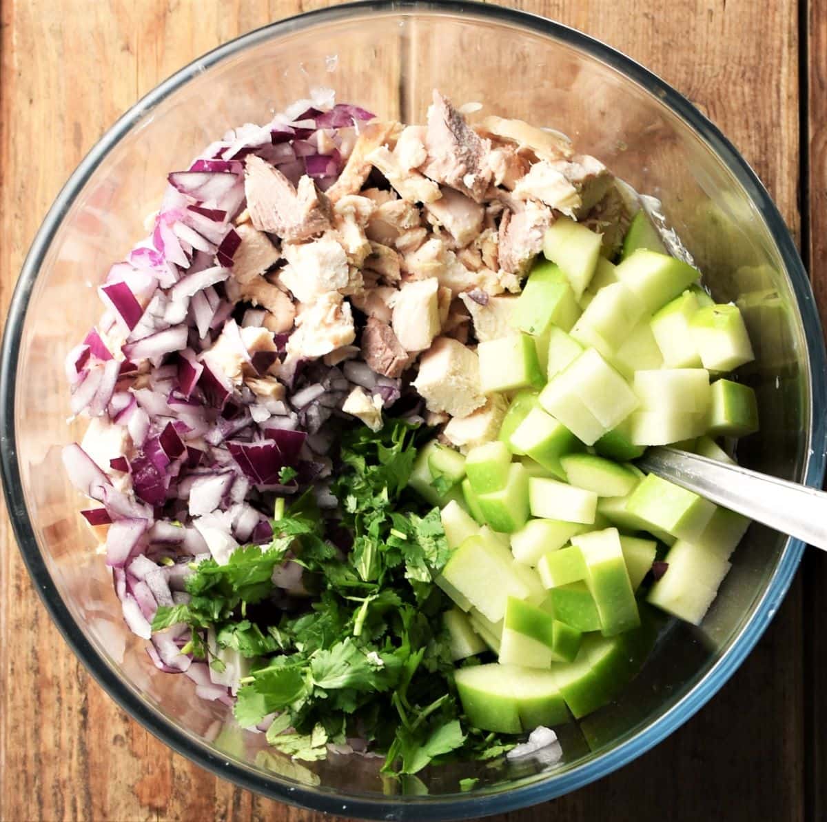 Chopped turkey, red onion, fresh herbs and apple in mixing bowl with spoon.