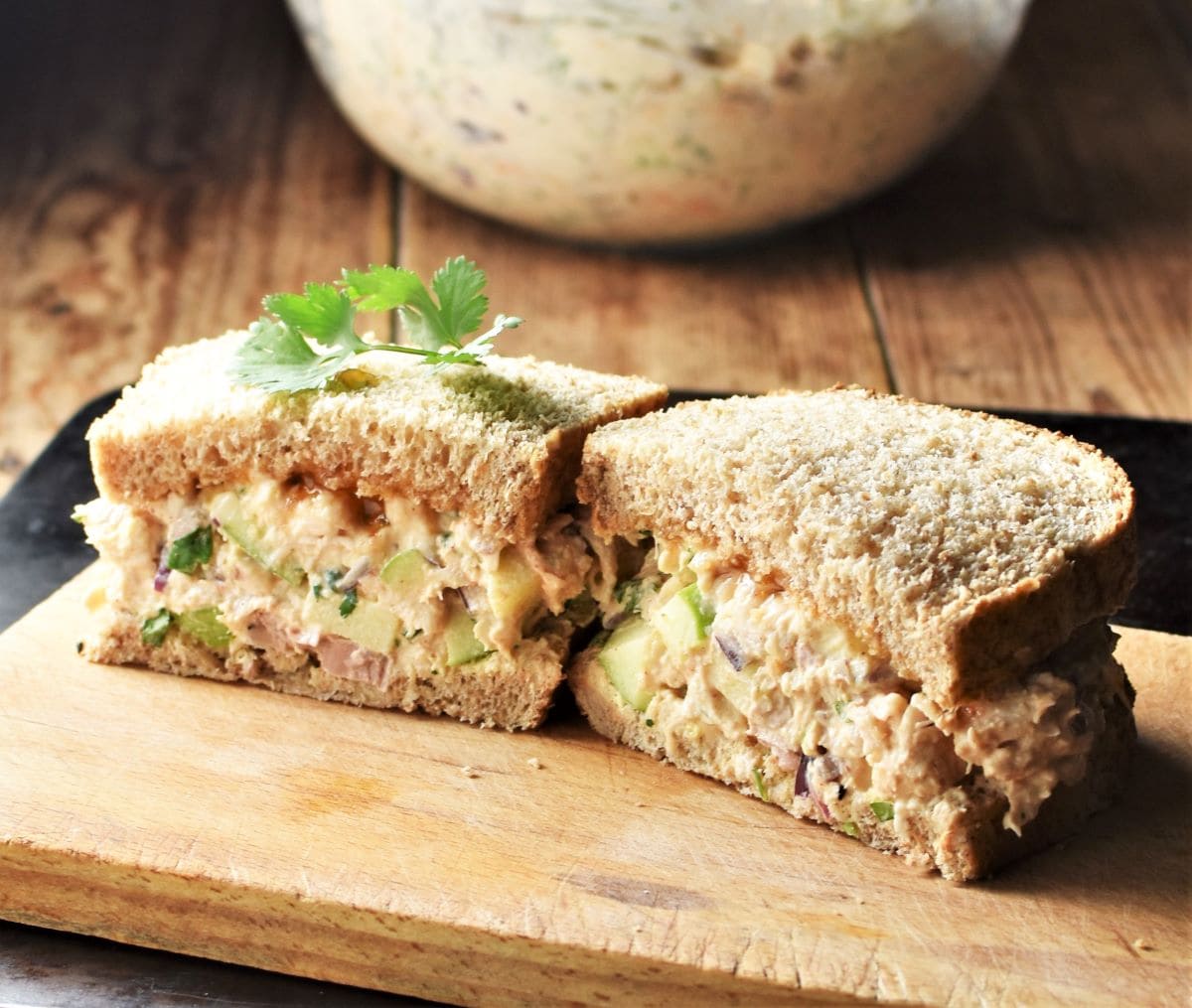 Side view of halved turkey salad sandwich on top of wooden board.