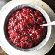Top down view of cranberry chutney in grey bowl with spoon on top of plate.