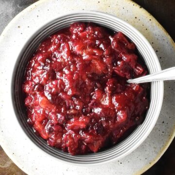 Top down view of cranberry chutney in grey bowl with spoon on top of plate.