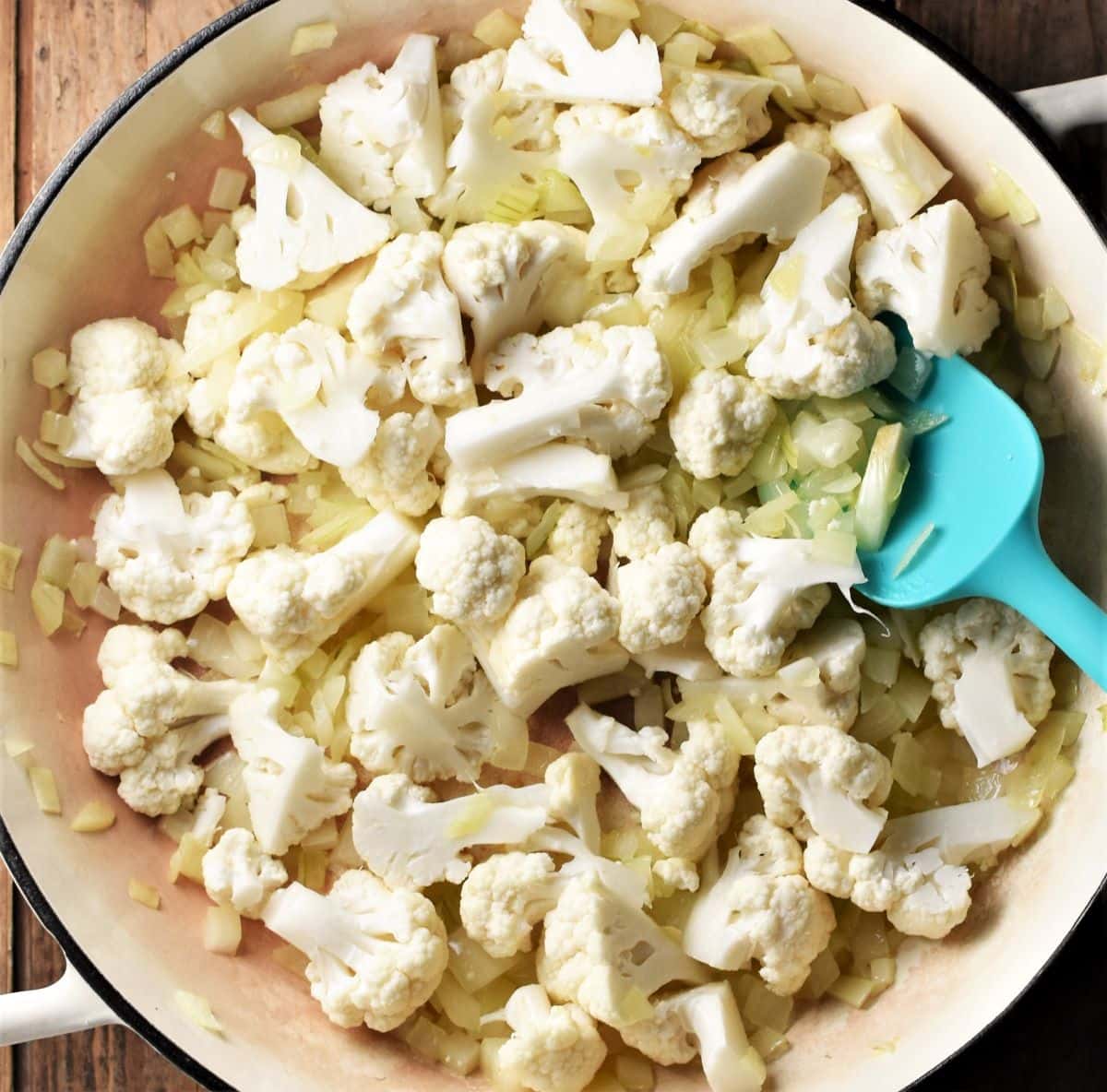 Chopped cauliflower in large pan with blue spoon.