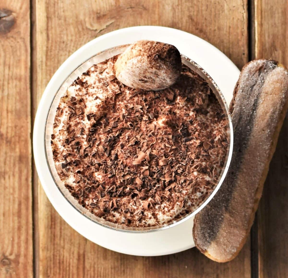 Top down view of tiramisu cup with ladyfinger on top of white saucer.