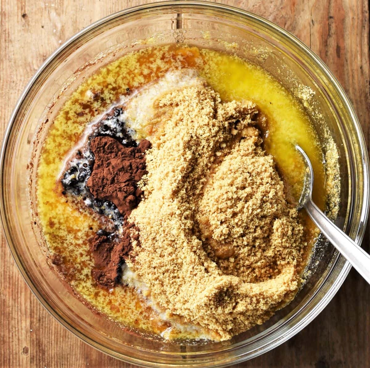 Biscuit crumb, cocoa and melted butter in bowl with spoon.
