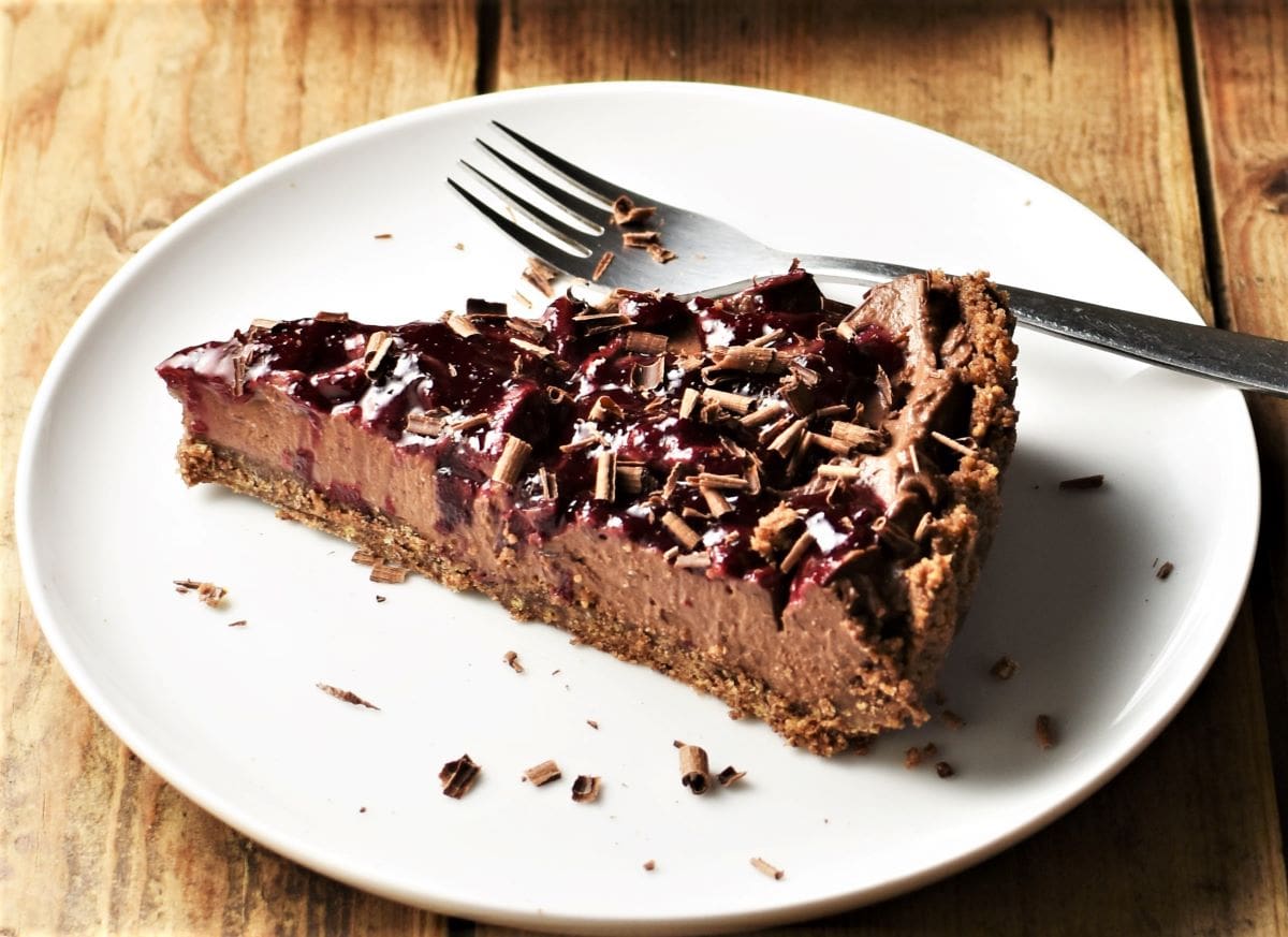 Side view of black forest cheesecake tart on white plate with fork.