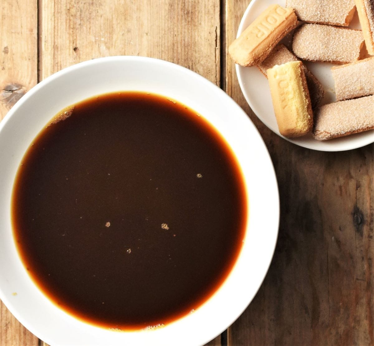 Coffee in bowl and ladyfingers on white plate.