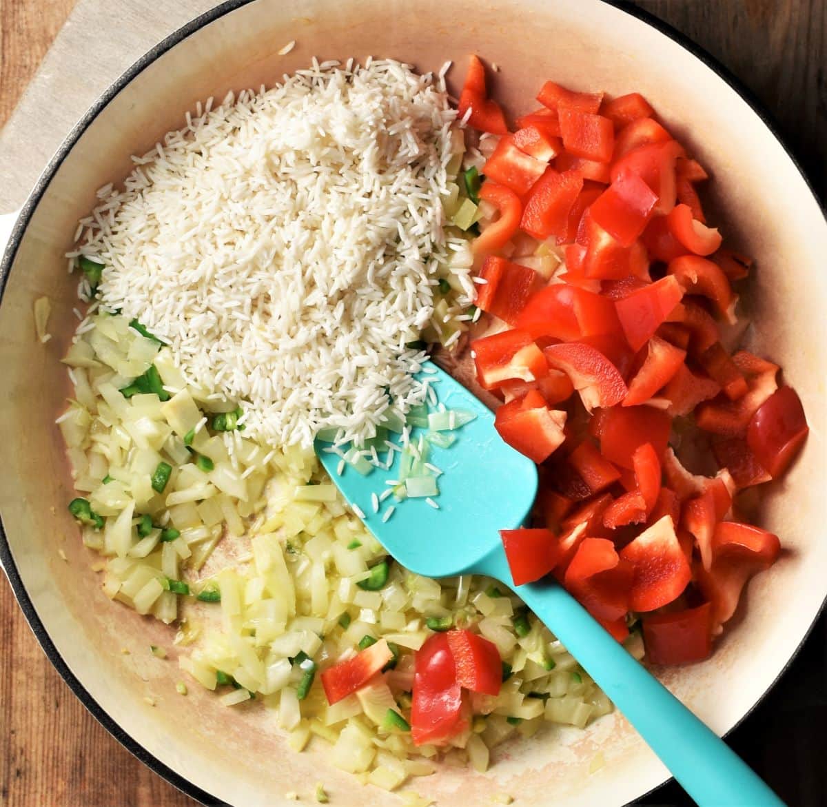 Rice, onion and red pepper in large shallow pan with blue spoon.