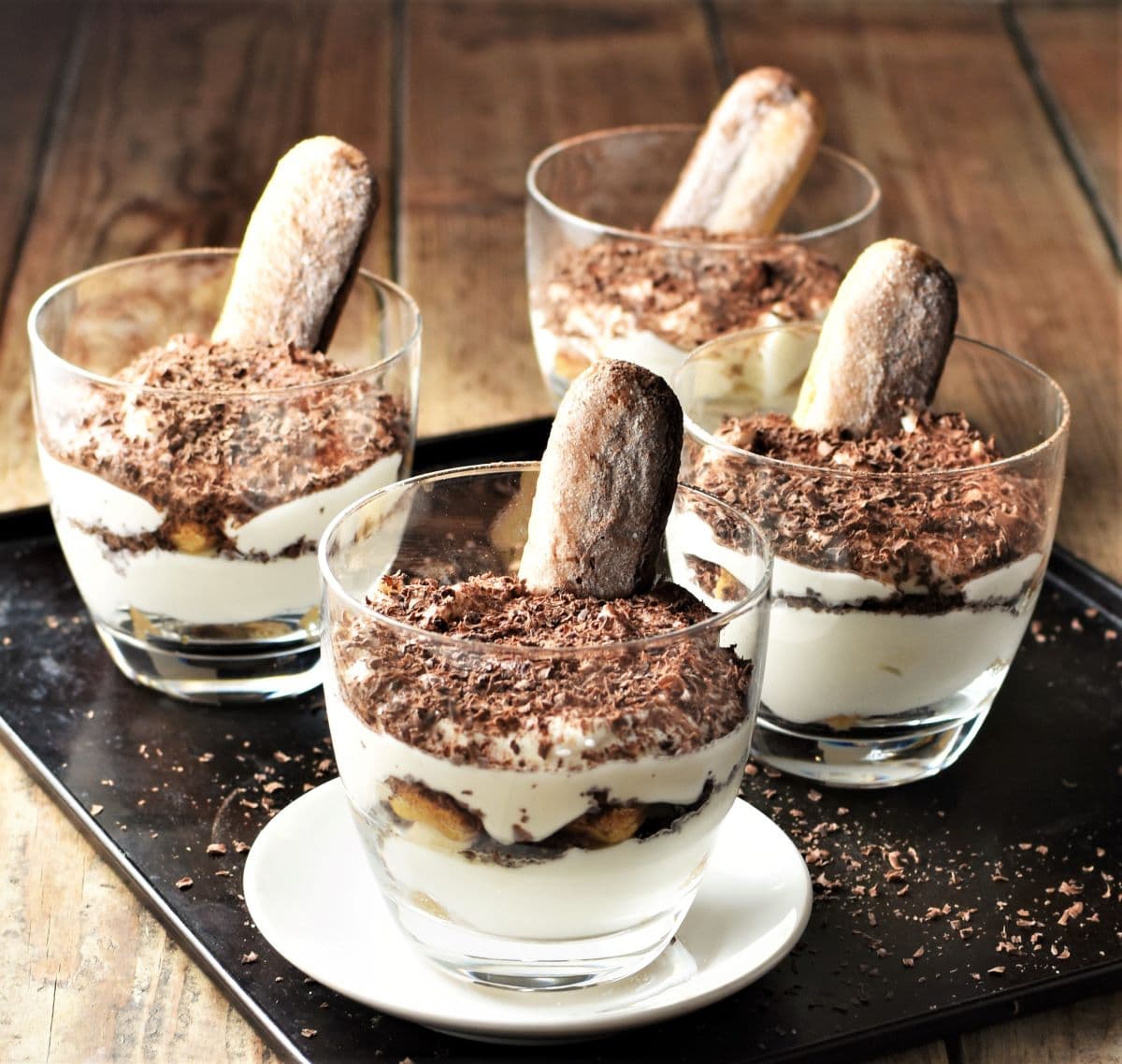 Side view of 4 tiramisu cups on black tray.