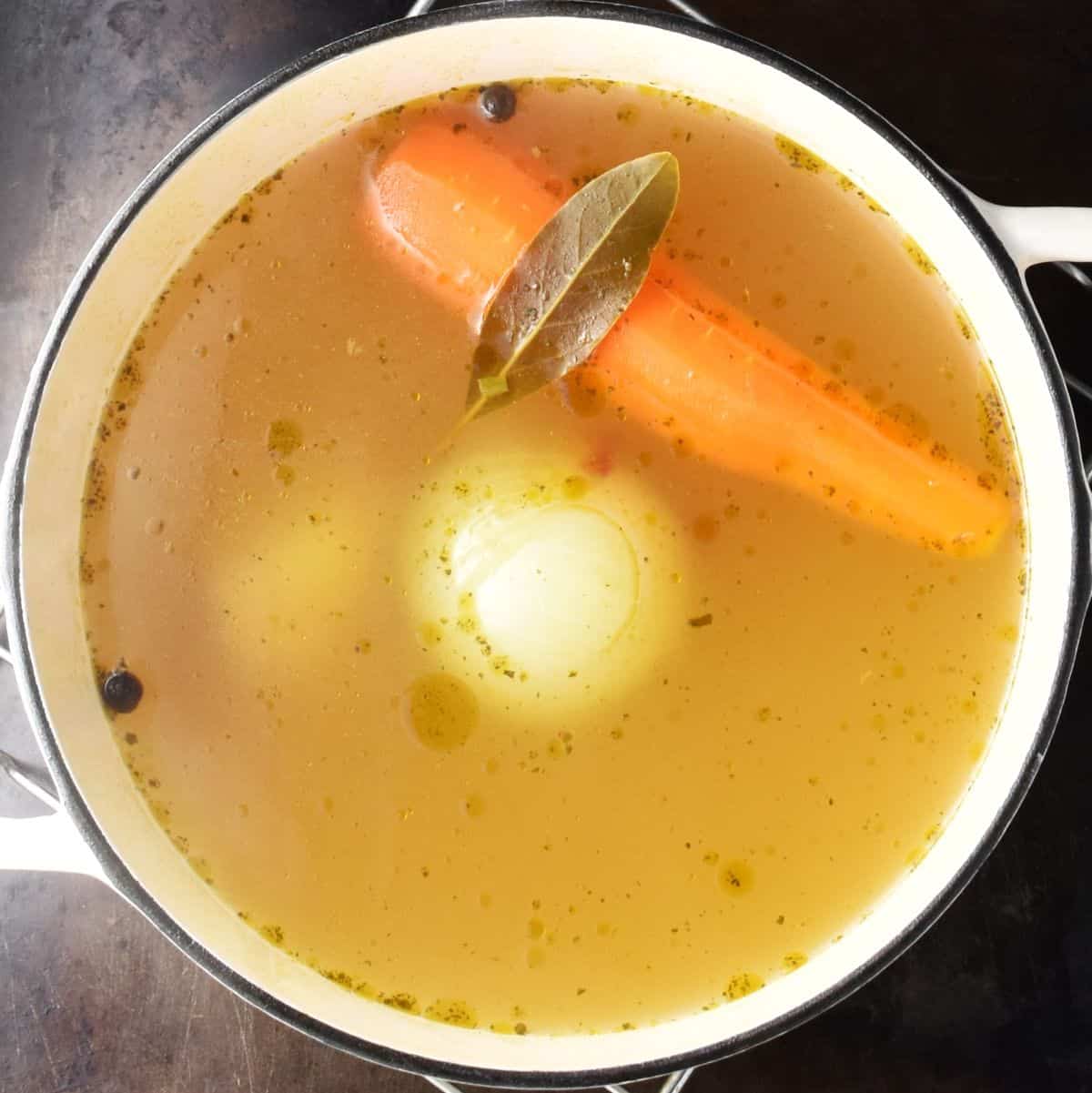 Top down view of vegetable stock for Polish Christmas wild mushroom soup with whole vegetables visible in white pot.