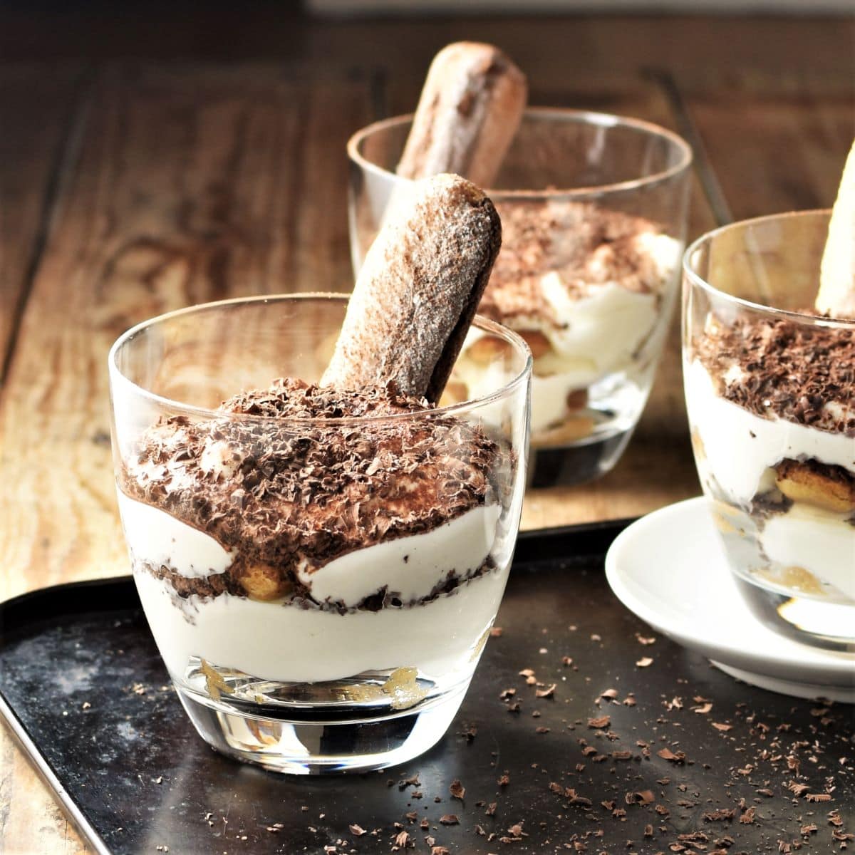 Side view of 3 mini tiramisu desserts with ladyfingers in cups.