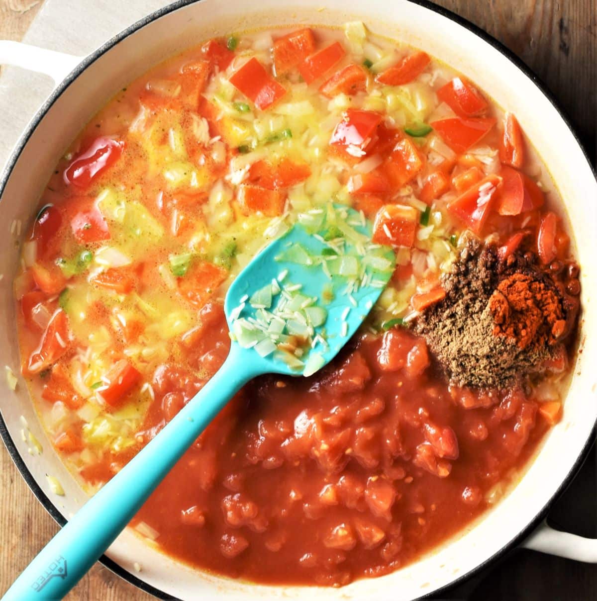 Tomatoes, rice and vegetable mixture in large pan with blue spoon.