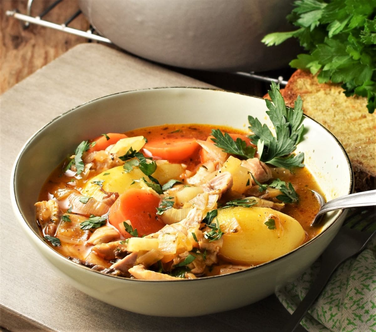Side view of potato and chicken stew with fresh herbs in green bowl.
