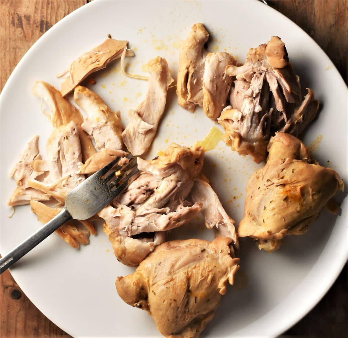 Shredding cooked chicken thighs with fork on top of plate.