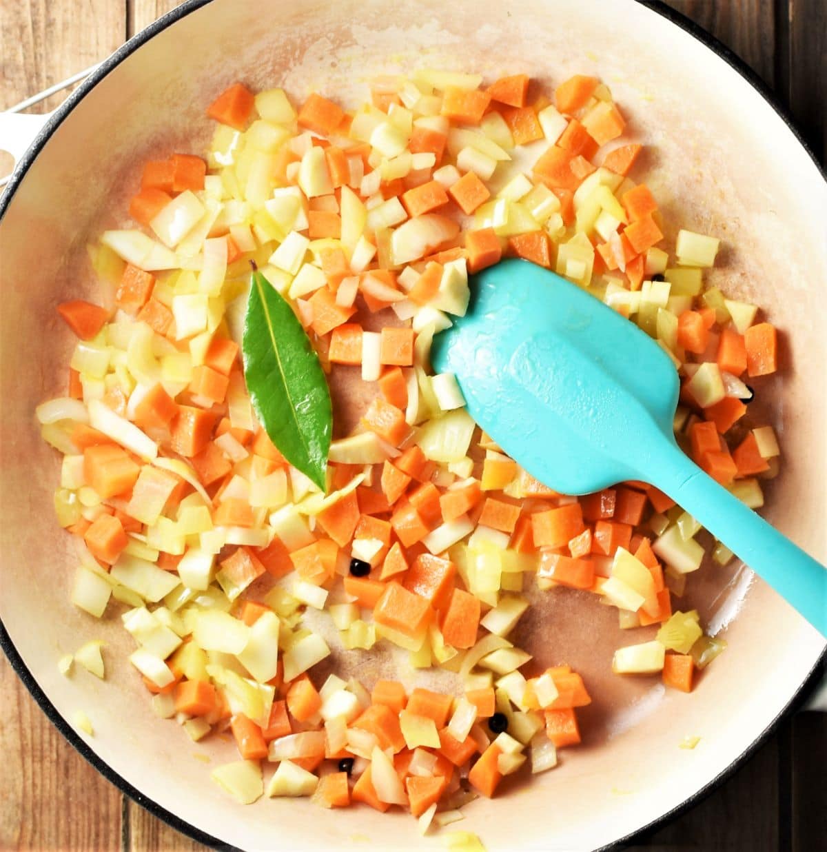Diced vegetables in large pan with blue spoon.