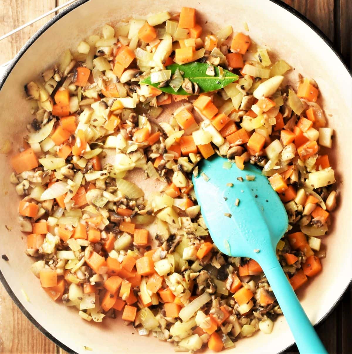 Diced vegetables and mushrooms in large pan with blue spoon.