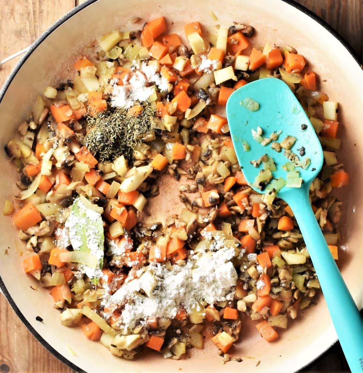 Diced vegetables, herbs and flour in large pan with blue spoon.