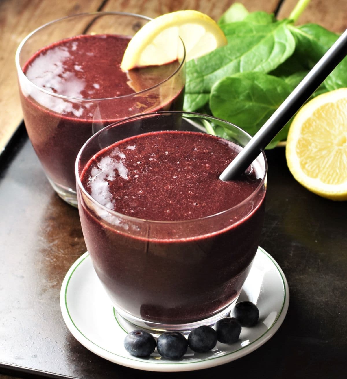 Spinach blueberry smoothie in 2 glasses with spinach and lemon in background.