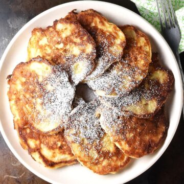 Top down view of crispy Polish apple pancakes dusted with powdered sugar on white plate.