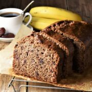 Side view of banana date bread with coffee cup and bananas in background.