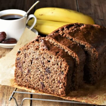 Side view of banana date bread with coffee cup and bananas in background.