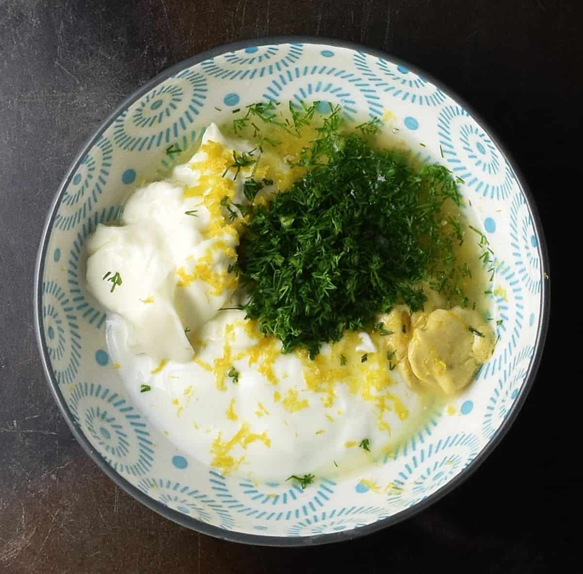Yogurt, mayo, mustard and fresh, chopped dill in small blue bowl.