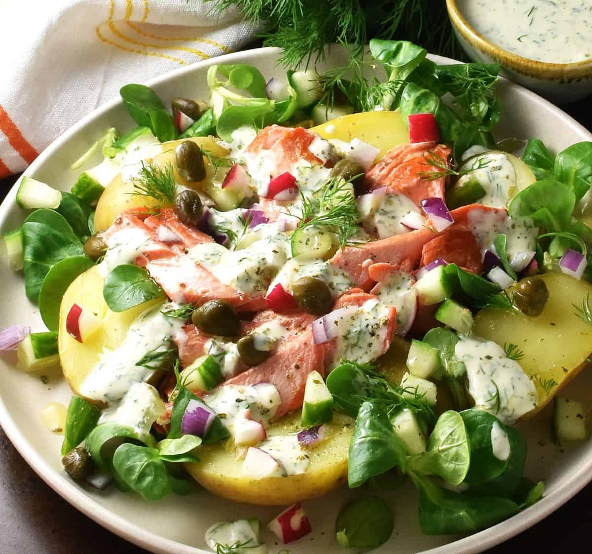Side view of potato and salmon salad with lettuce and dressing on white plate.