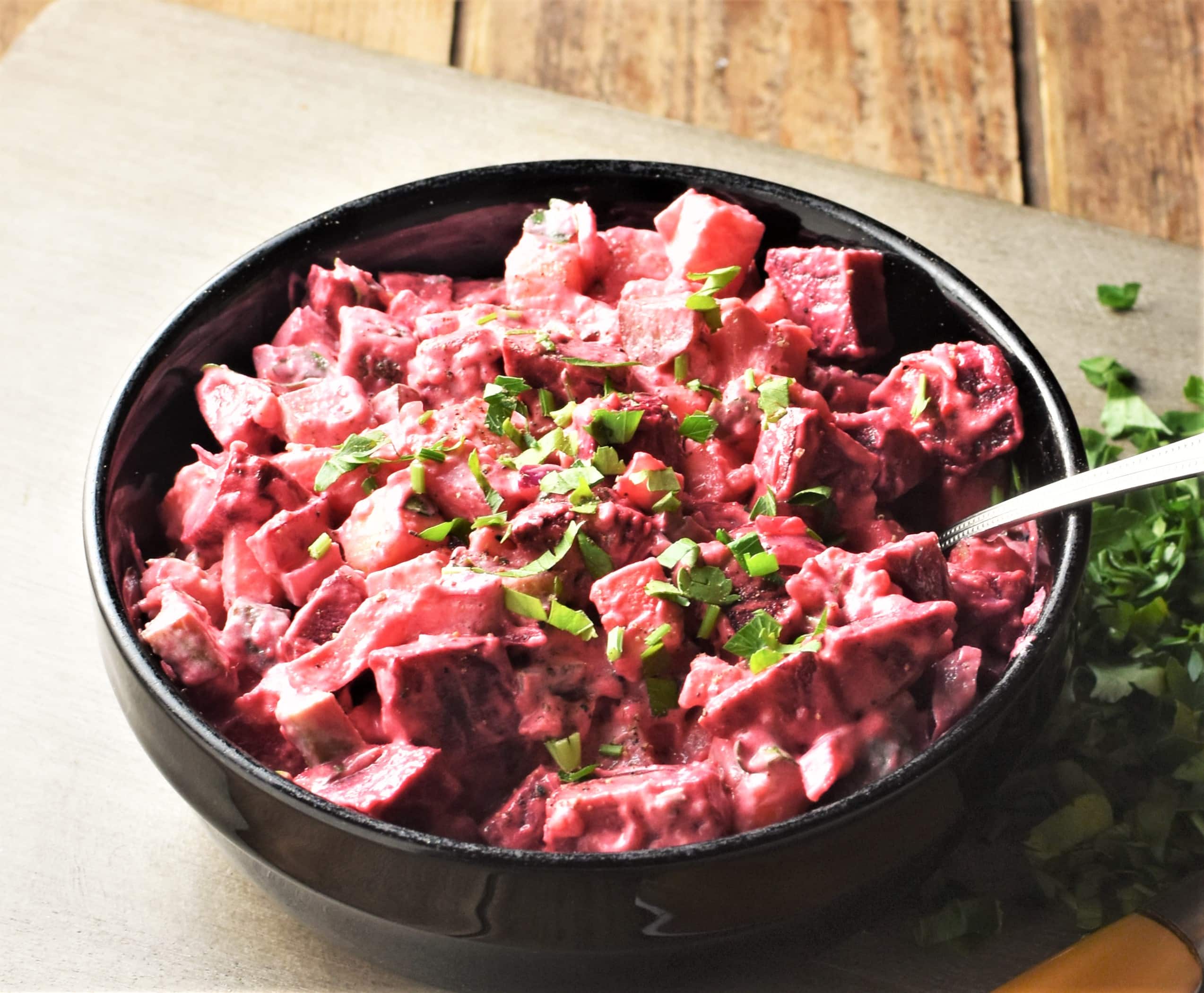 Side view of potato beet salad in black bowl with spoon.