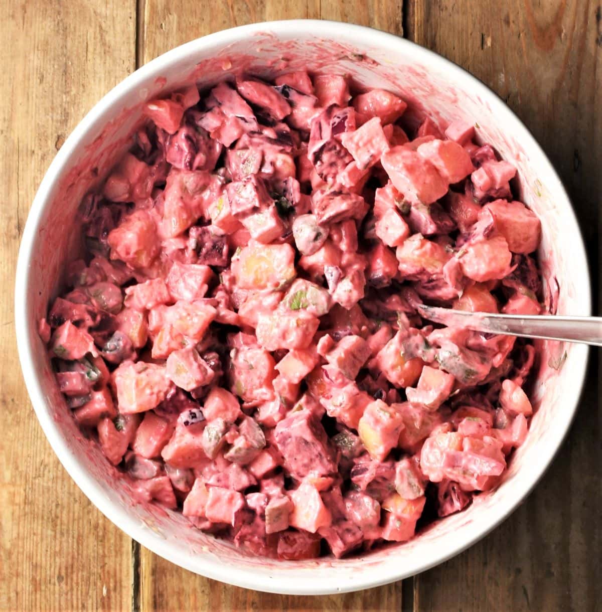Potato beet salad in white mixing bowl with spoon.