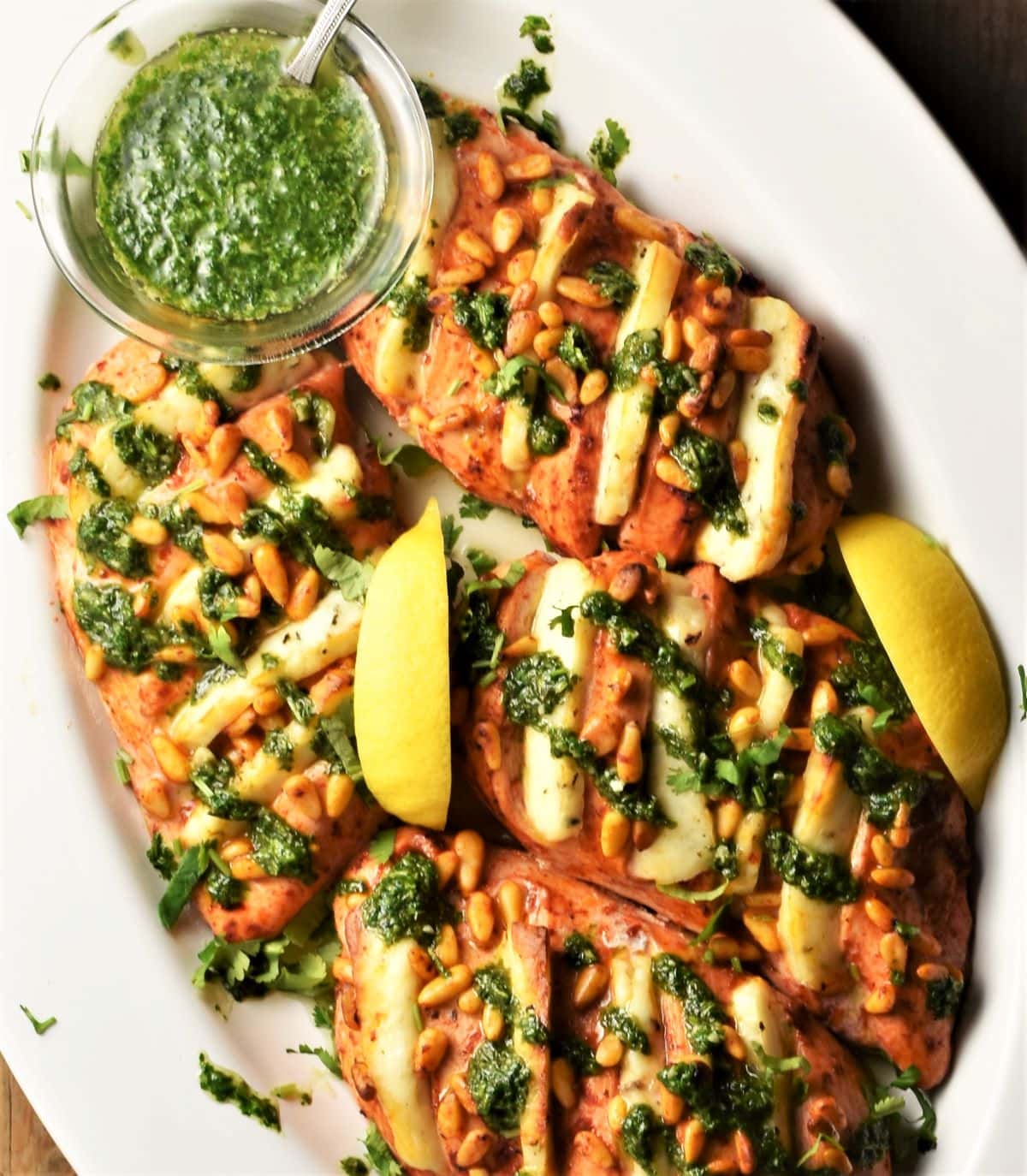 Top down view of hasselback halloumi chicken with cilantro sauce and lemon in oval dish.