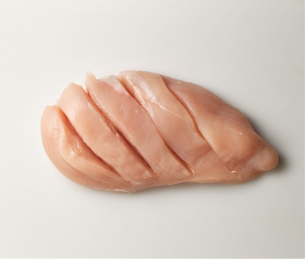 Hasselbacked raw chicken breast on top of white board.