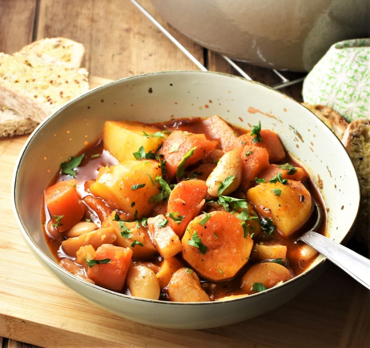 Side view of root vegetable stew in green bowl with spoon and bread in background.