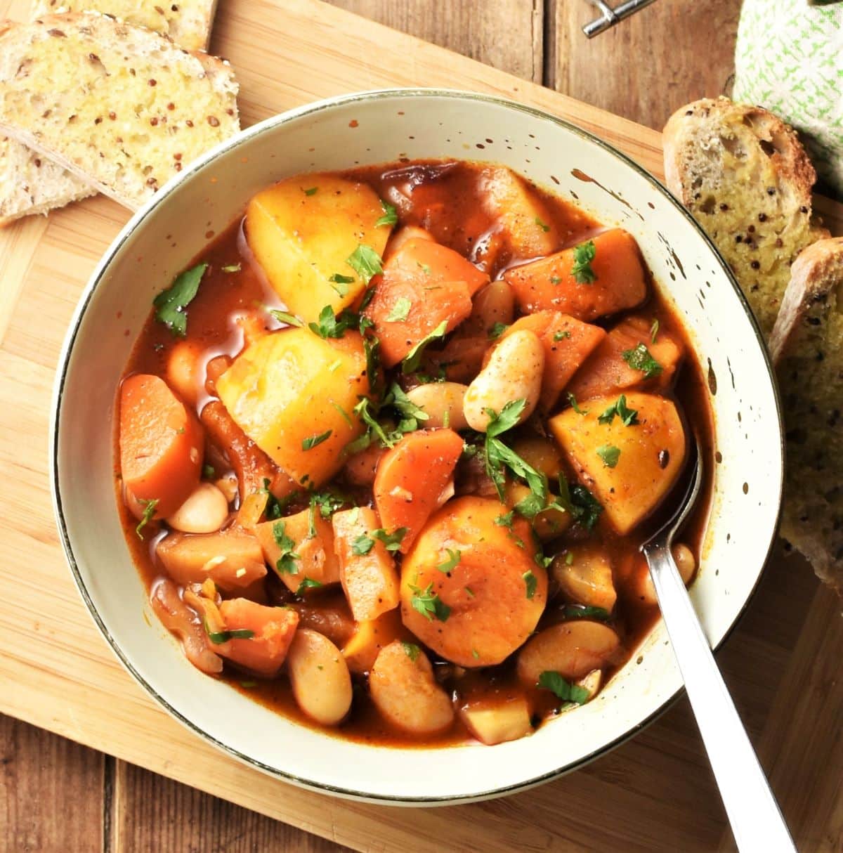 Chunky root veg stew in green bowl with spoon and bread in background.
