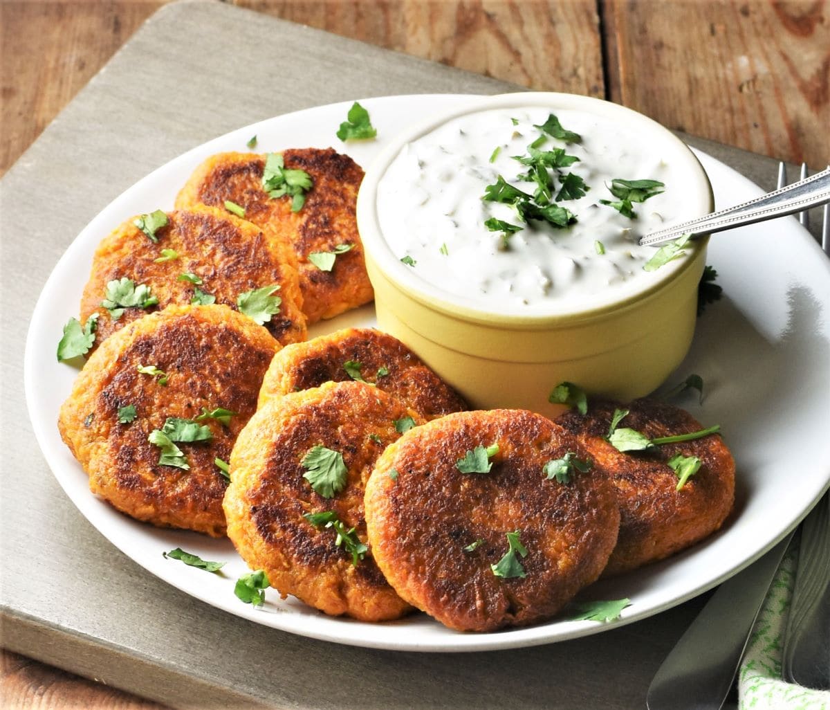Side view of sweet potato cakes on top of plate with yogurt dip in the middle.