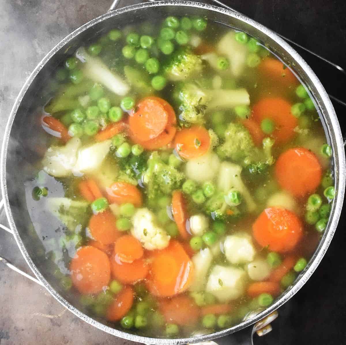 Cooked soup with chunks of vegetables on top in large pot.