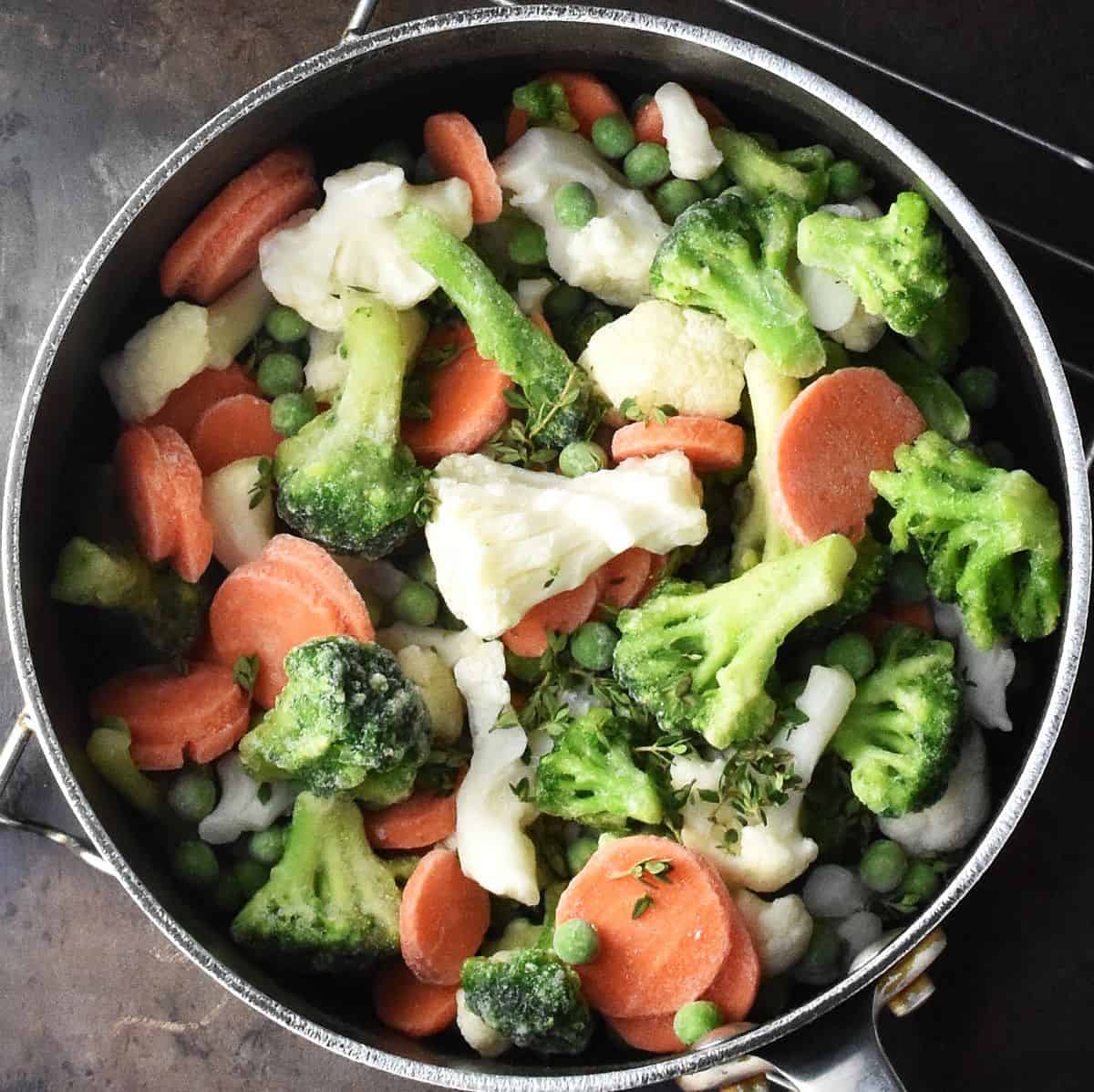 Top down view of frozen cauliflower, broccoli and carrot pieces in pot.