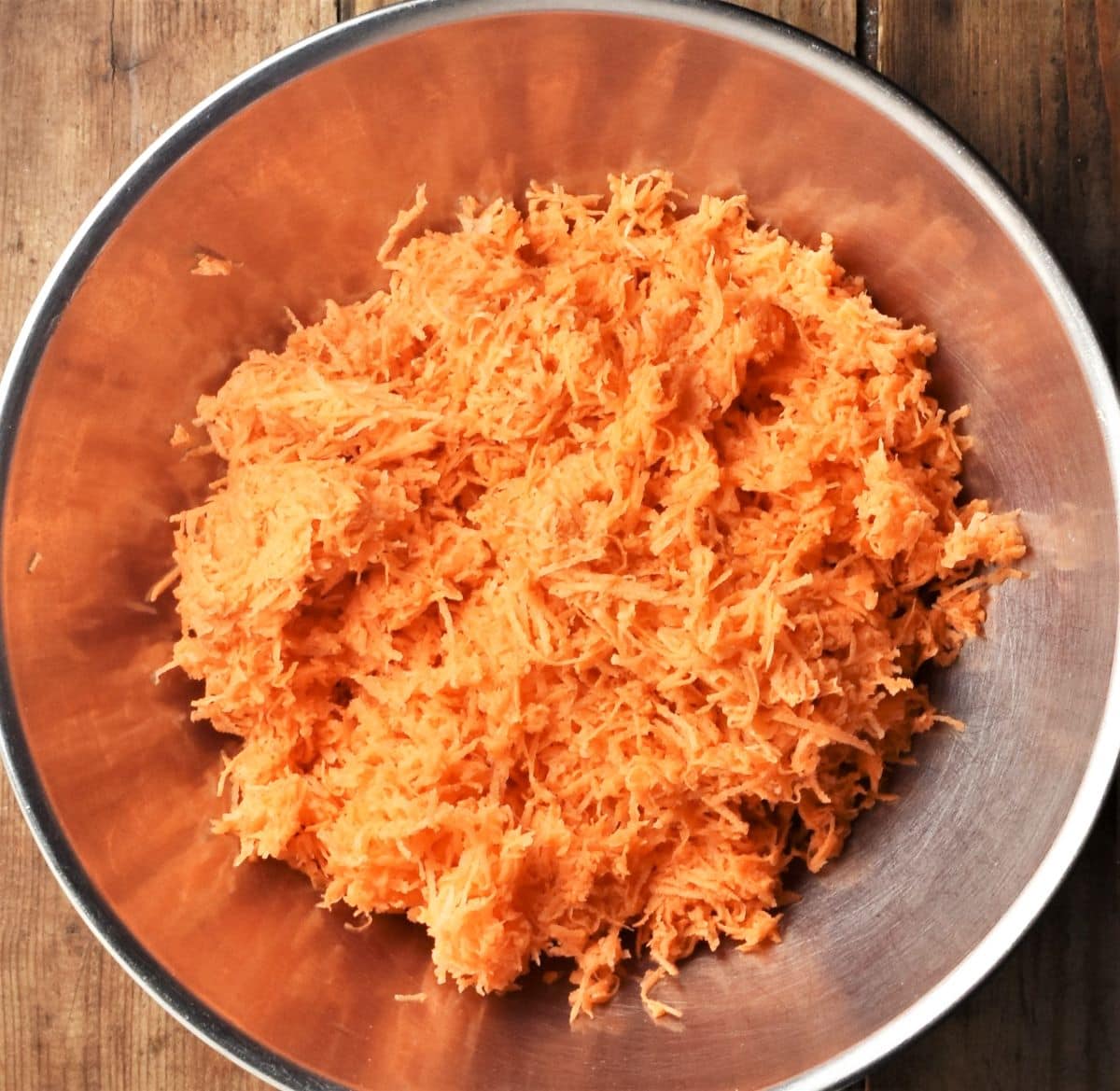 Finely grated sweet potato for making fritters in metal bowl.