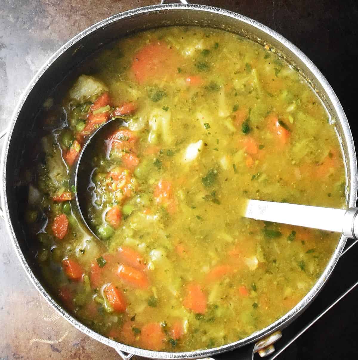 Partly pureed soup with frozen veg in large pot with ladle.