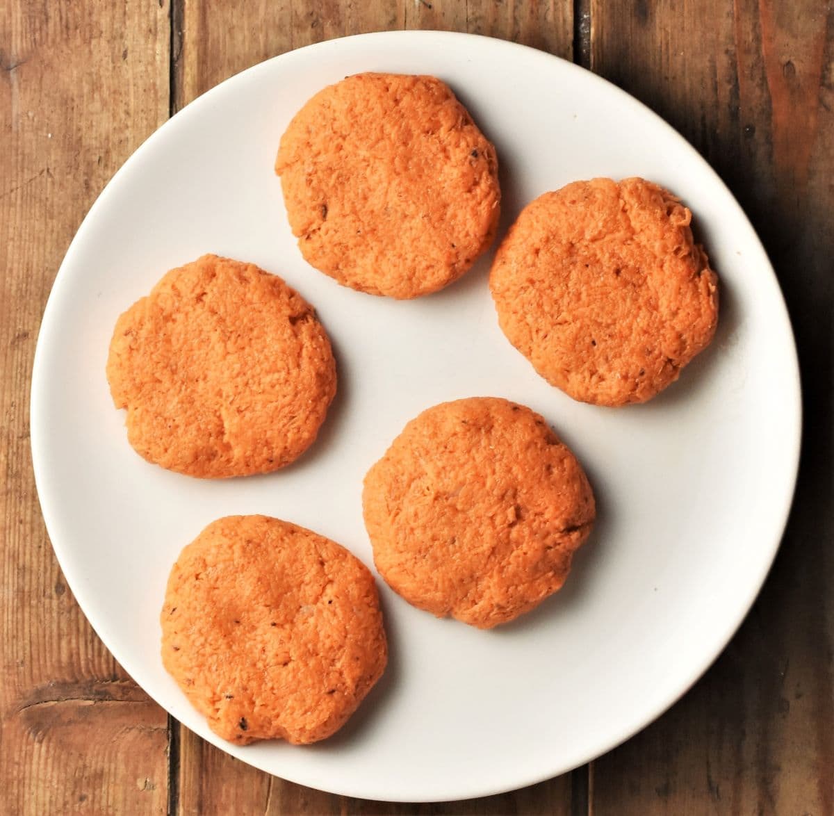 5 uncooked sweet potato cakes on top of white plate.