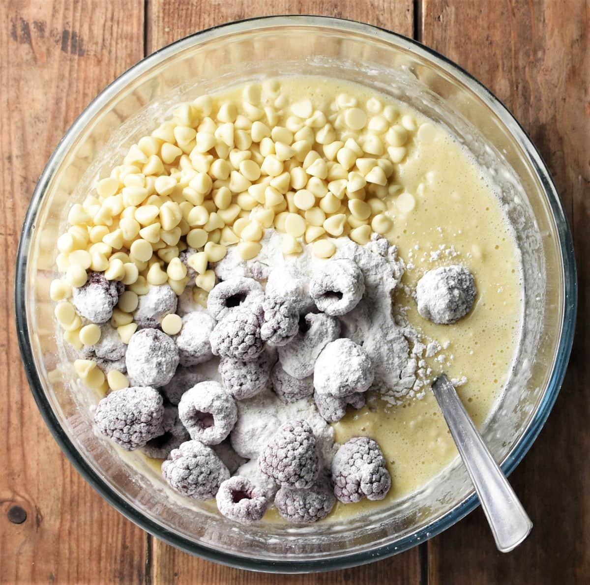 Muffin batter with white chocolate chips and raspberries in mixing bowl.
