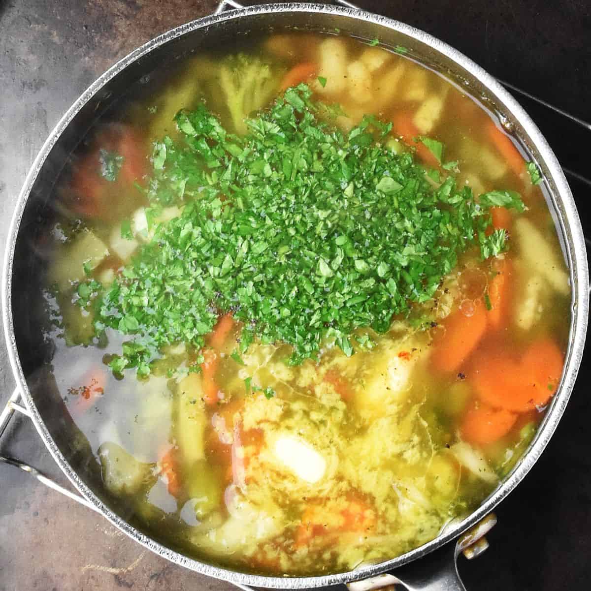 Top down view of chunky veg soup with fresh herbs on top in large pot.