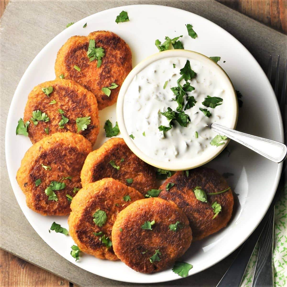 Top down view of sweet potato fritters on white plate with yogurt dip.