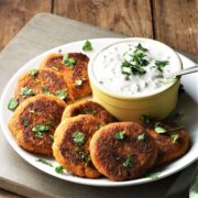 Side view of sweet potato fritters on top of plate with yogurt dip in yellow dish.