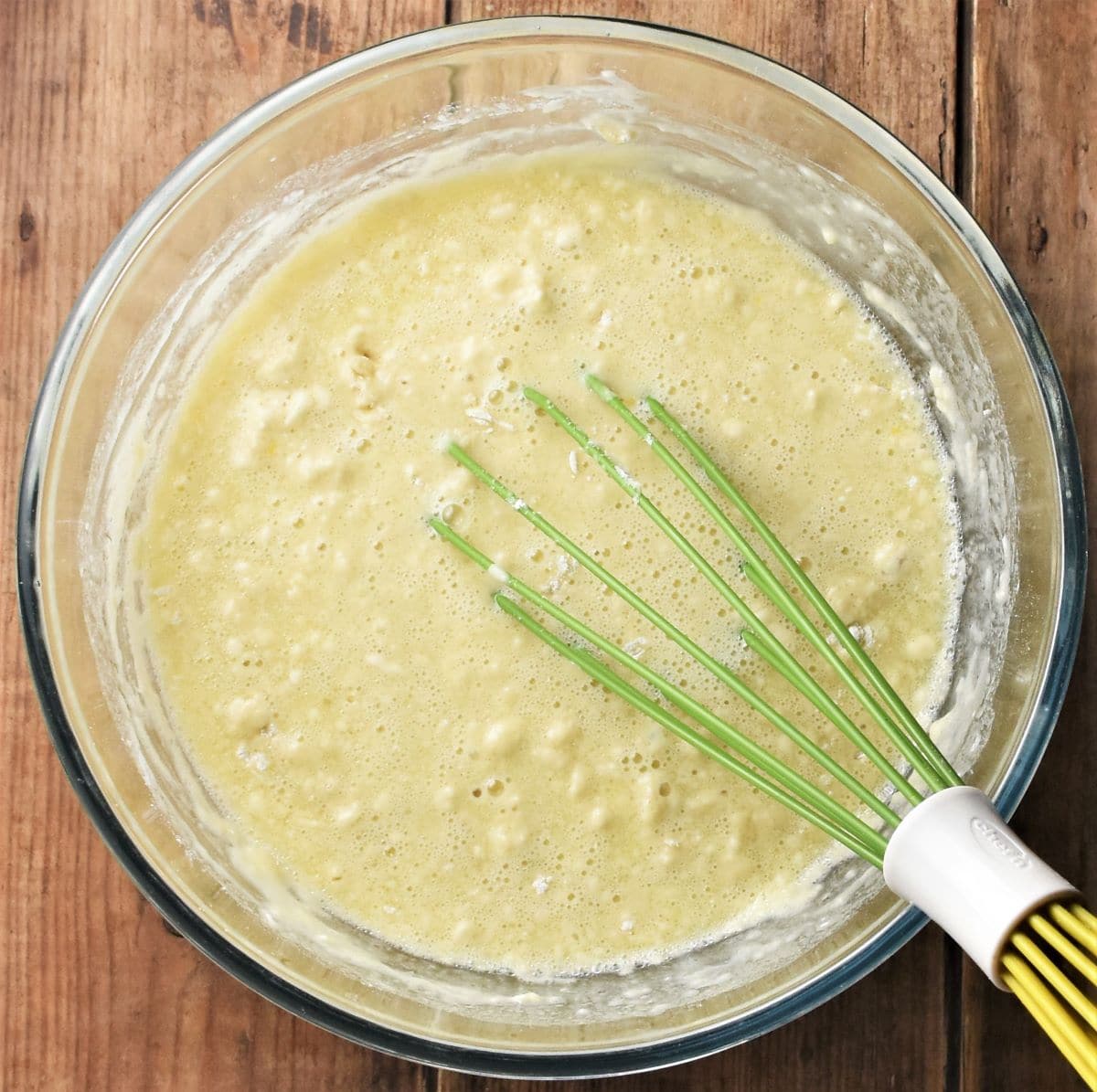 Muffin batter in mixing bowl with green whisk.